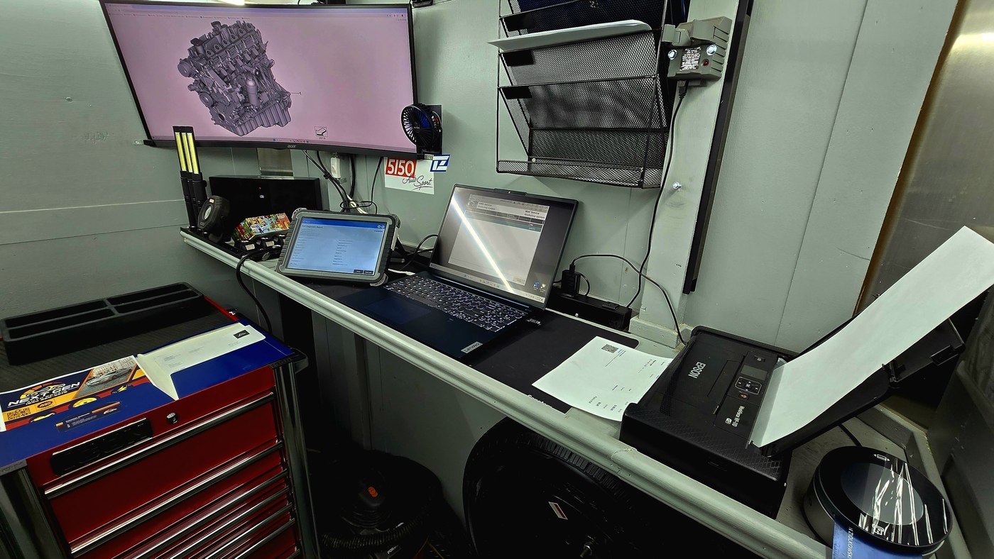 Workbench with diagnostic scanners, laptop, and engine 3D model on the trailer monitor
